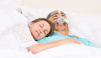 Woman sleeping next to man wearing C P A P machine